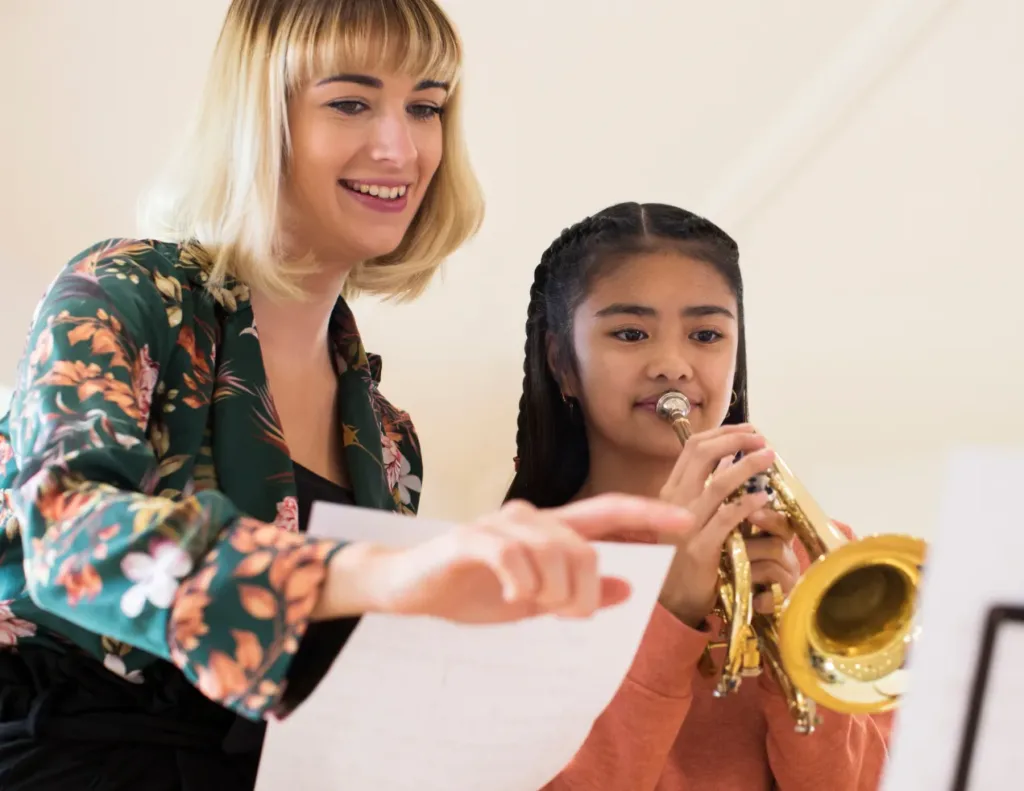 A teacher demonstrating proper breathing techniques and embouchure to a young student playing a wind instrument, such as a flute or clarinet.
