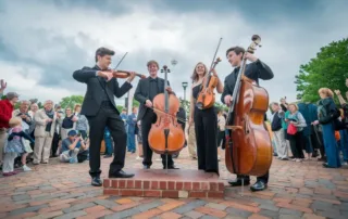 A dynamic photo of a student string quartet performing in an outdoor plaza, with a diverse crowd gathered around them, capturing the joy and engagement on both performers' and audience members' faces