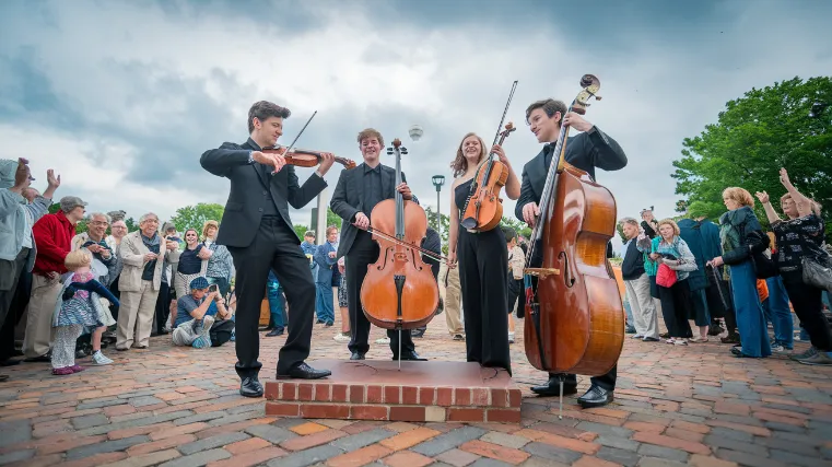 A dynamic photo of a student string quartet performing in an outdoor plaza, with a diverse crowd gathered around them, capturing the joy and engagement on both performers' and audience members' faces